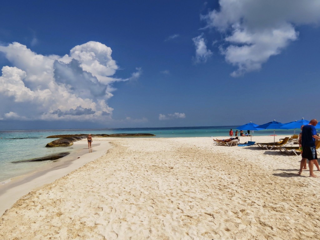 Wit zandstrand in Mexico met ligbedden en blauwe parasols aan helderblauw zeewater.