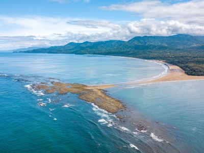 een baai met zandstrand, rotsen in zee en groene bergen aan de kust van Costa Rica.