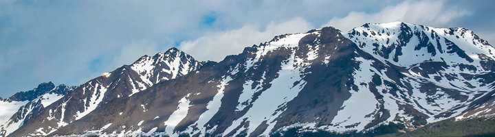 Besneeuwde bergtoppen bij Ushuaia in Patagonië onder een blauwe lucht.