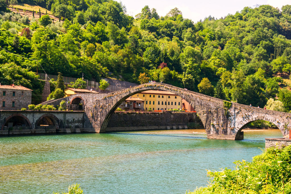 Middeleeuwse stenen boogbrug over een rivier in Toscane, omringd door groene heuvels.