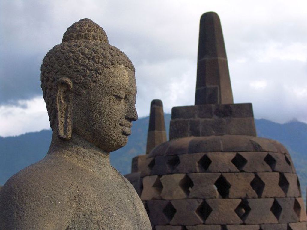 Boeddhabeeld bij de Borobudur-tempel op Java, Indonesië, met stupa’s en bergen op de achtergrond.