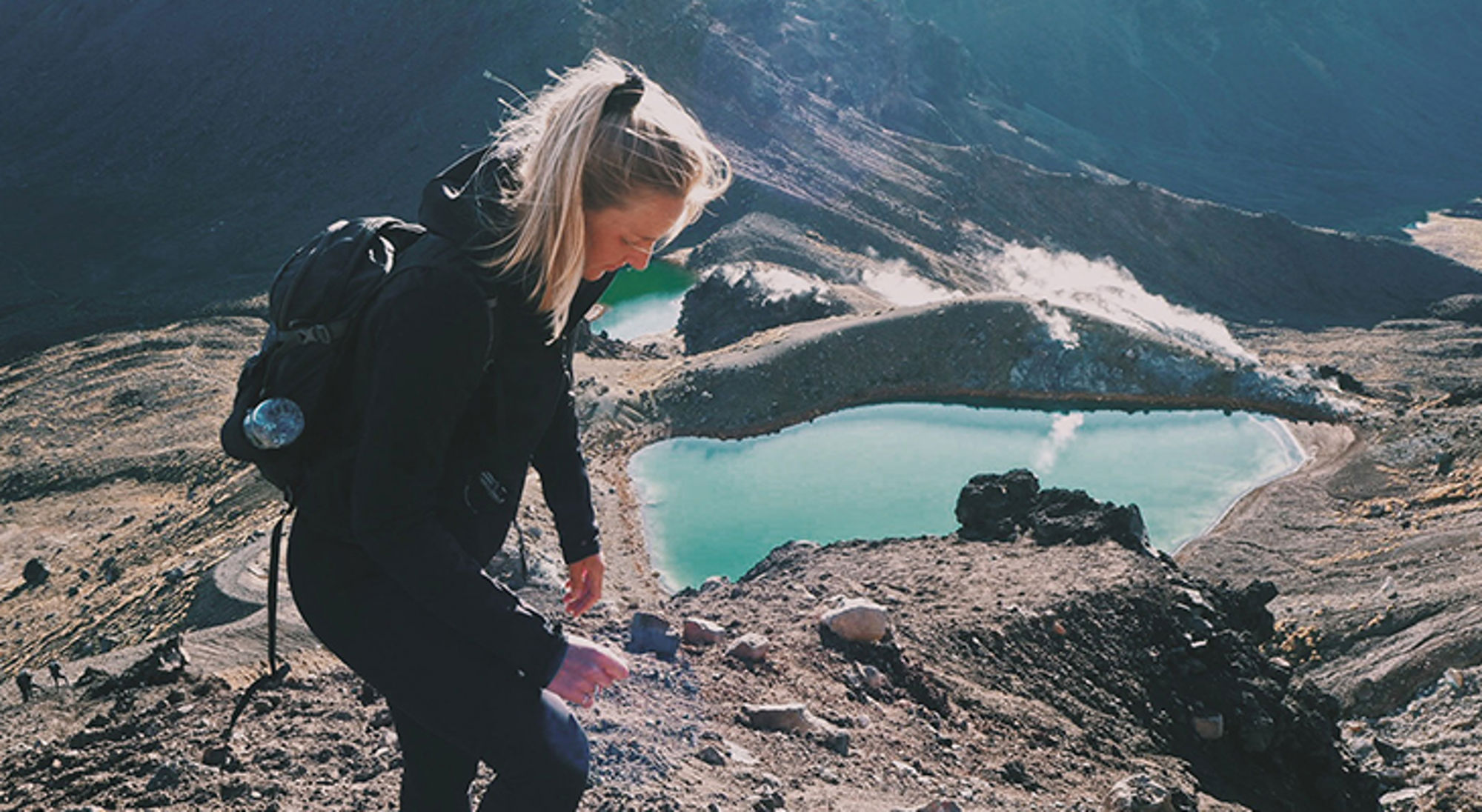 Wandelaar op bergkam met uitzicht op turquoise kratermeren in vulkanisch landschap.