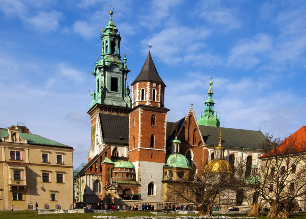 Wawelkathedraal in Krakau, Polen, met groene torens en gouden koepel onder een blauwe lucht.