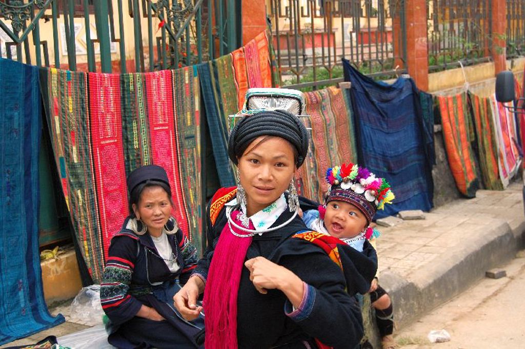 Vrouw met baby in traditionele kleding bij kleurrijke stoffen op een markt in Vietnam tijdens een groepsrondreis.