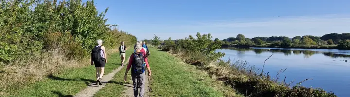 Wandelaars met rugzakken op een dijkpad langs een rivier tijdens onze eerste groepsreis in Nederland.