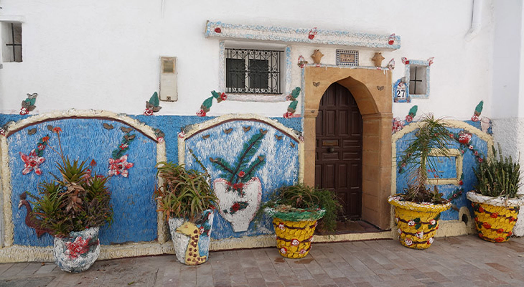 Rabat Marokko Witte gevel met blauwe muurschilderingen, boogdeur en kleurrijke bloempotten.
