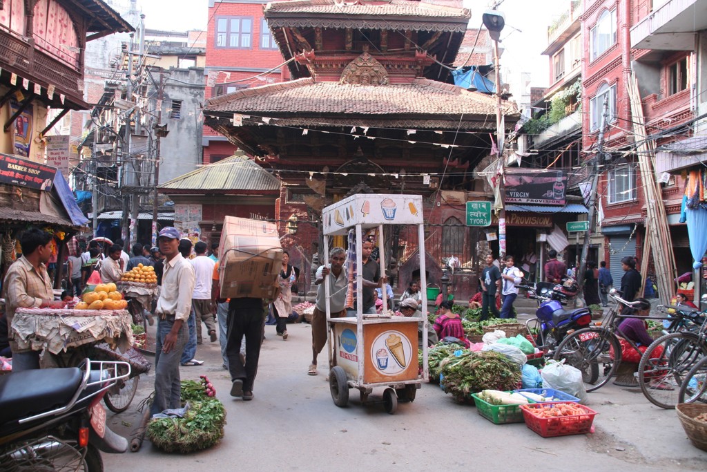 Drukke straatmarkt in Kathmandu met groenteverkopers en een tempel op de achtergrond tijdens een groepsrondreis Noord-India en Nepal.
