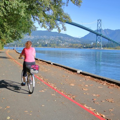 Fietser op de Seawall in Vancouver met uitzicht op de Lions Gate Bridge en de bergen.