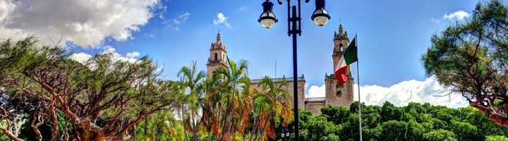 Kleurrijk Merida-bord op Plaza Grande met de kathedraal van Mérida en de Mexicaanse vlag op de achtergrond.