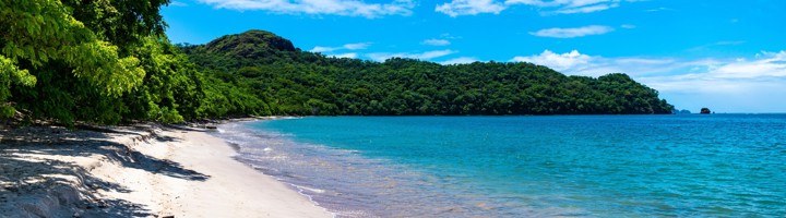 Witte zandstrand en helderblauw water bij Playa Conchal in Costa Rica, met groene heuvels op de achtergrond.