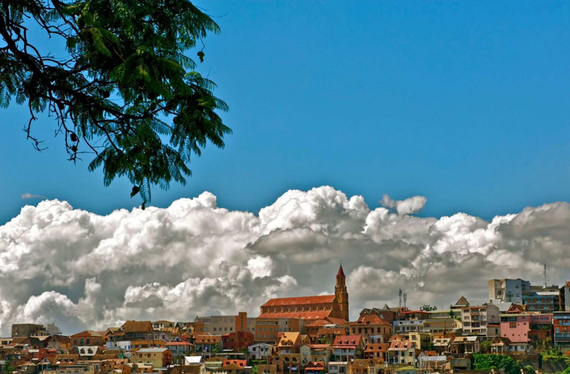 Skyline van Antananarivo met kerk en kleurrijke huizen onder een blauwe lucht met wolken.