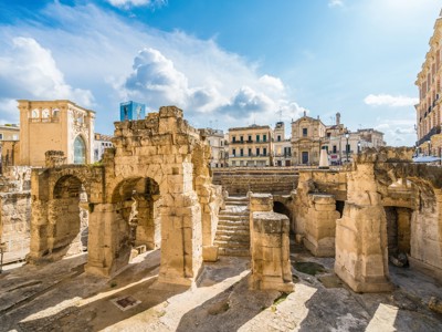 Romeinse ruïnes en bogen in Lecce, Puglia, met historisch stadsplein op de achtergrond.