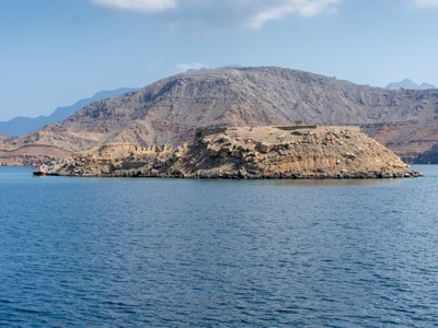 Rotseiland en bergen aan de kust van Oman, gezien vanaf het water tijdens de route Oman en Dubai.