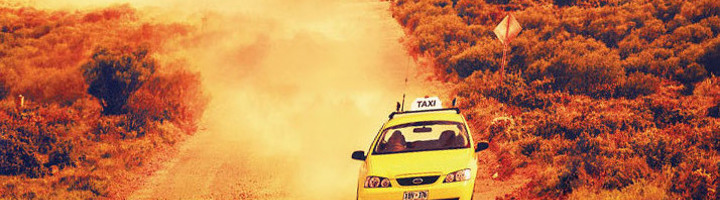 Gele taxi rijdt over stoffige outbackweg in Australië.