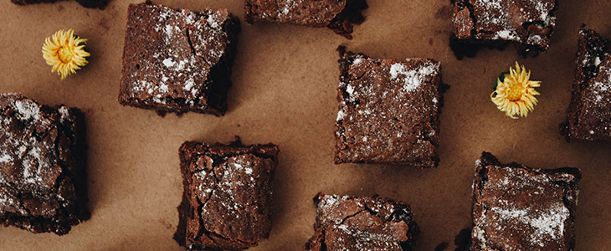 Brownies met poedersuiker op bakpapier, met gele bloemen als decoratie.