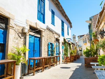 Sfeervol straatje in Cyprus met stenen huizen, blauwe luiken en terrassen in de zon.