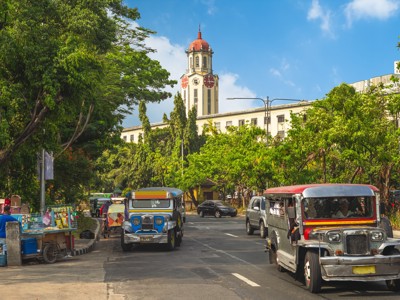 Jeepneys rijden door Manila met de klokkentoren van het Manila City Hall op de achtergrond.