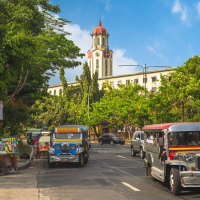 Jeepneys rijden door Manila met de klokkentoren van het Manila City Hall op de achtergrond.