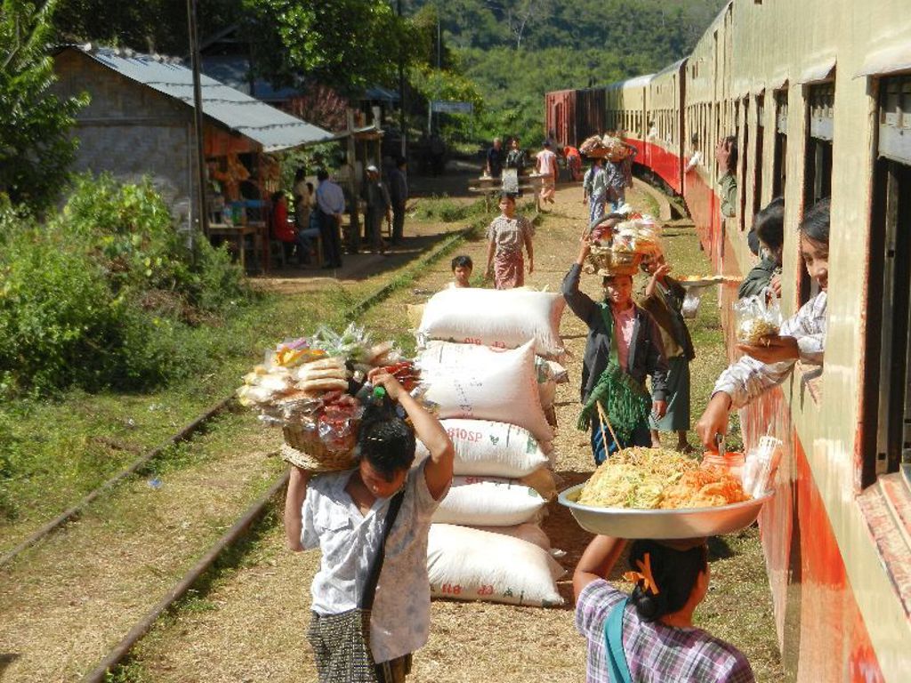 Verkopers met eten lopen langs de trein op een station in Myanmar tijdens een groepsrondreis.
