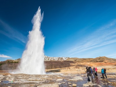 Geysir die hoog water de lucht in spuit in IJsland, met reizigers op afstand.