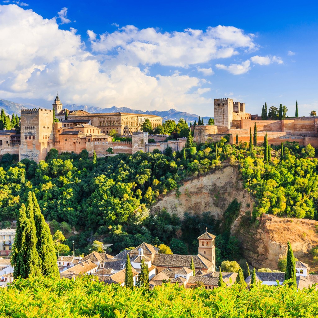 Alhambra in Granada, Andalusië, met paleismuren en torens boven groene heuvels en de Sierra Nevada.