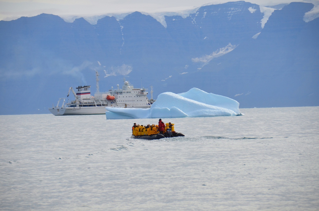 Zodiacboot met reizigers bij een ijsberg in Disko Bay, Groenland, met expeditieschip op de achtergrond.