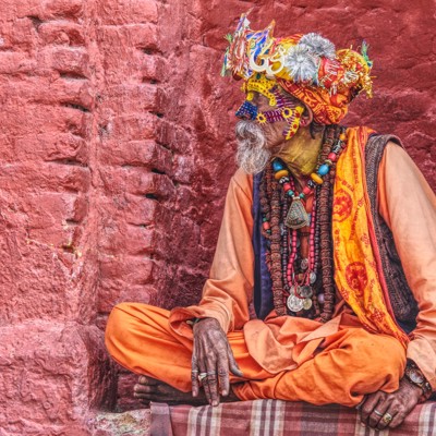Sadhu in kleurrijke kleding en sieraden zit tegen een rode muur in Nepal.