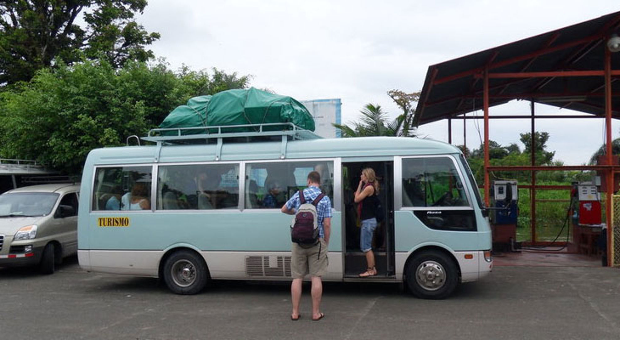 Bus vervoer San Jose Toeristen stappen in een minibus met bagage op het dak bij een tankstation in Costa Rica.