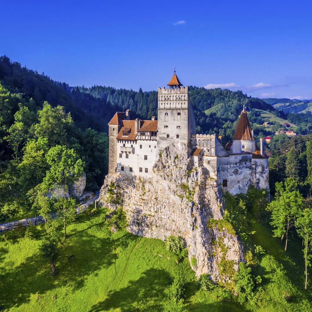 Kasteel Bran in Transsylvanië, Roemenië, op een rots met groene heuvels en bossen eromheen.