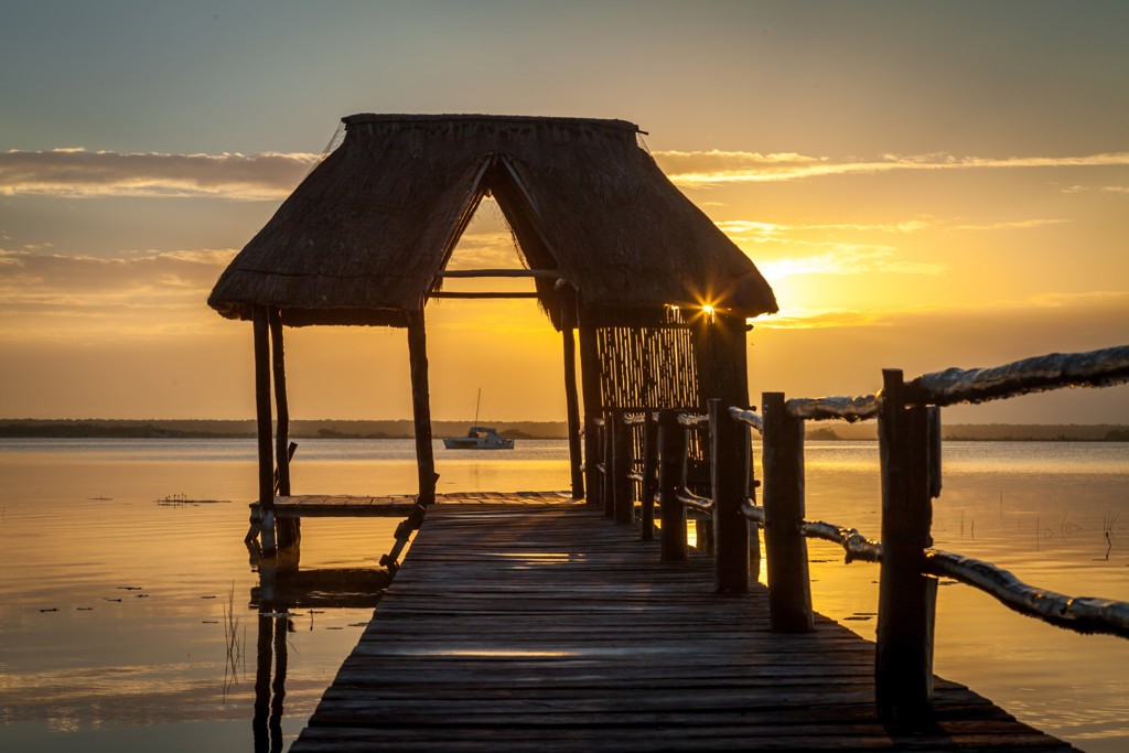 Houten steiger met rieten afdak bij zonsondergang aan een lagune in Mexico.