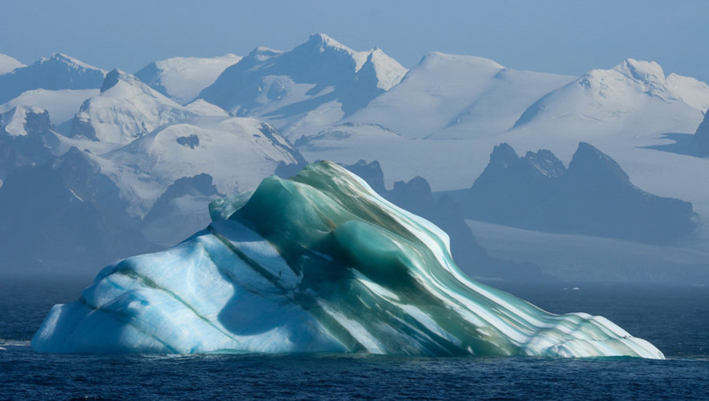 Drijvende ijsberg voor besneeuwde bergen in Antarctica tijdens een groepsrondreis per boot.