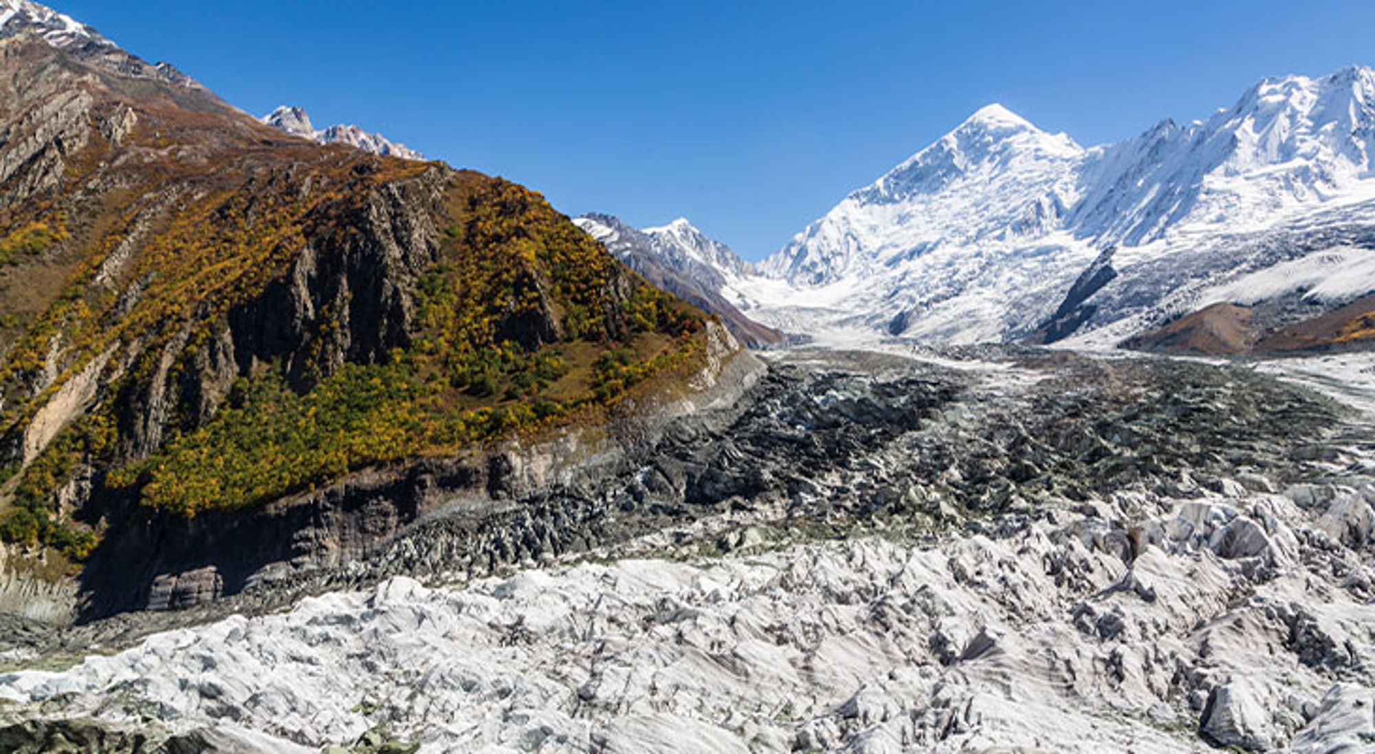 Minapin gletsjer Pakistan Uitzicht op een gletsjer met besneeuwde bergtoppen en rotsachtige hellingen onder een heldere blauwe lucht.