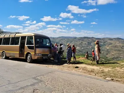 Minibus langs de weg in Madagascar met reizigers en locals bij een uitkijkpunt over heuvels.