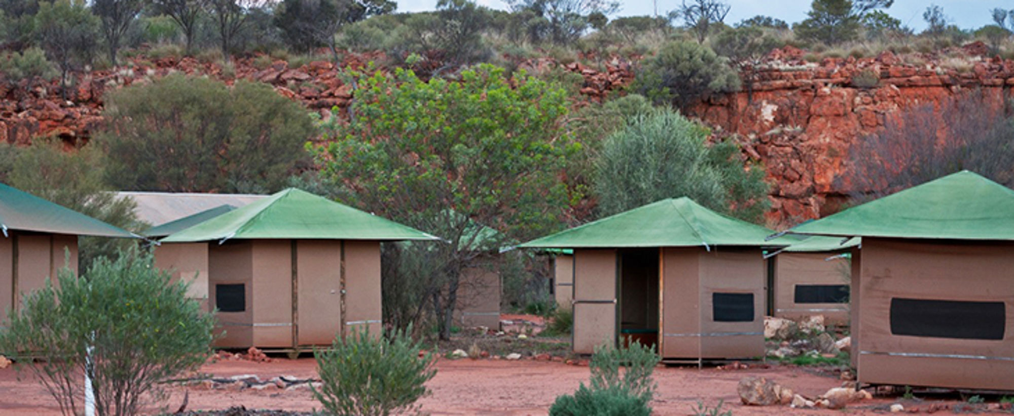 Safaritenten in Australië Safaritenten met groene daken bij rood rotslandschap en struiken.