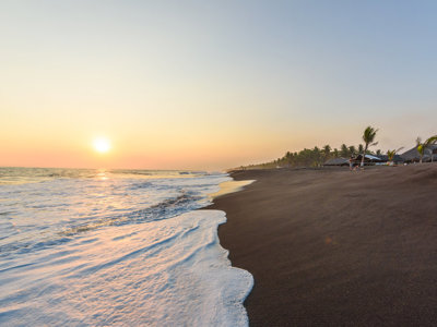 Zonsondergang aan een zwart zandstrand aan de Pacifische kust van Guatemala, met palmbomen en golven.