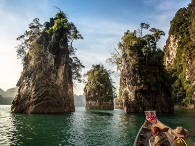 Longtailboot vaart tussen kalkstenen rotsformaties op een groenblauw meer in Thailand.