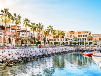 Boulevard in Aqaba aan de Rode Zee met palmbomen, hotels en een kleine jachthaven.