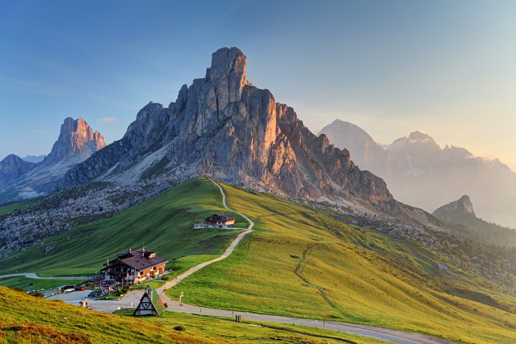 Berglandschap in Centraal Europa met groene alpenweide, berghutten en rotsmassief in avondlicht.