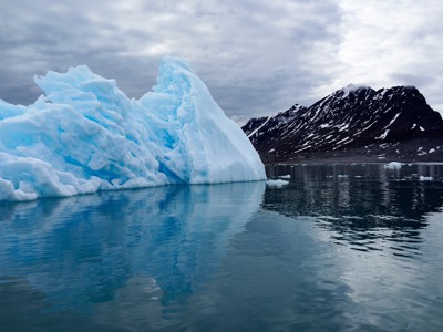 Blauwe ijsberg in rustig water bij de bergen van Spitsbergen.