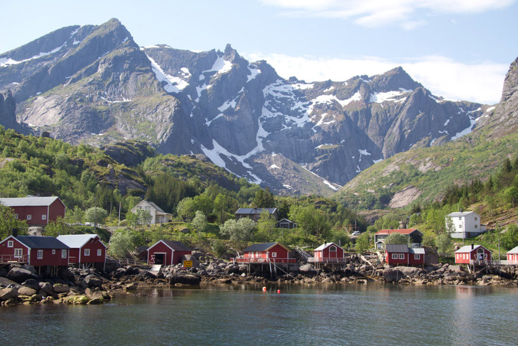 Rode vissershuisjes aan een fjord met groene bergen en besneeuwde toppen op de Faeröer eilanden.