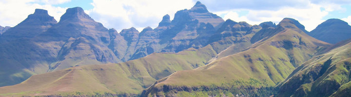 Panorama van de Drakensberg met groene berghellingen en rotsige pieken onder een blauwe lucht.