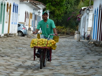 Fruitverkoper op fiets in een koloniale straat met kleurrijke gevels, route Buenos Aires naar Rio.