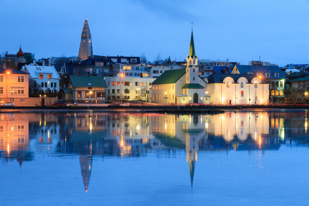 Avondzicht op Reykjavik met Hallgrímskirkja en kerk aan het water, weerspiegeld in de baai.