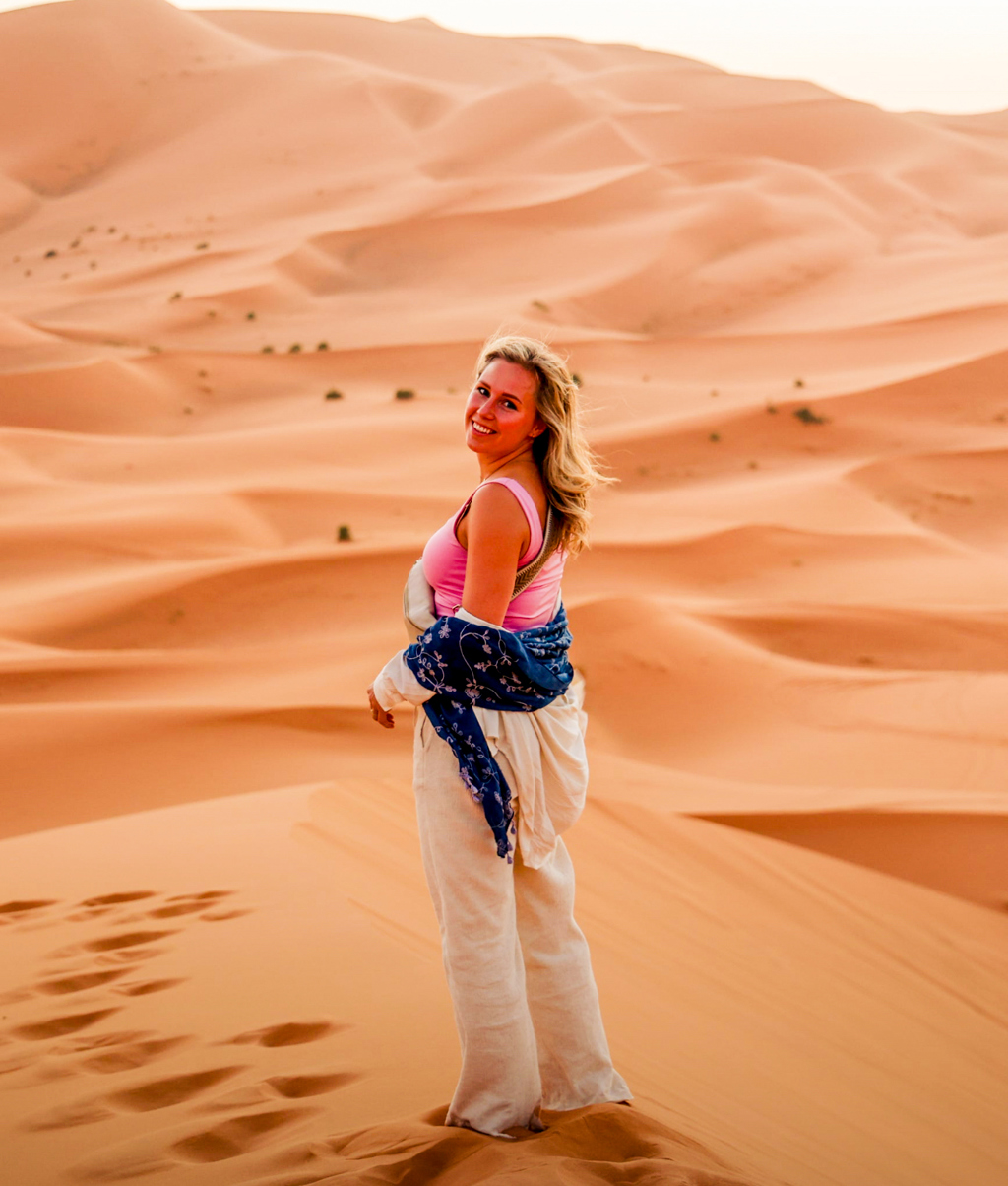 Reiziger in de Sahara bij Merzouga tijdens 22-35ers reis Marokko, met zandduinen op de achtergrond.
