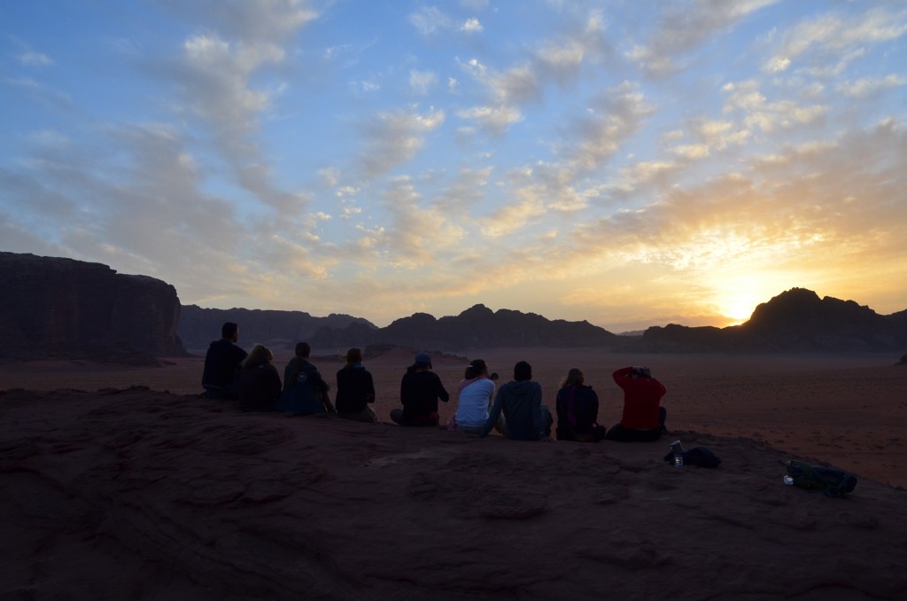 Groep reizigers kijkt naar de zonsopkomst in de Wadi Rum-woestijn in Jordanië.