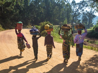 Lokale vrouwen en een kind lopen over een zandweg met manden op het hoofd tijdens de route Kenia & Tanzania.