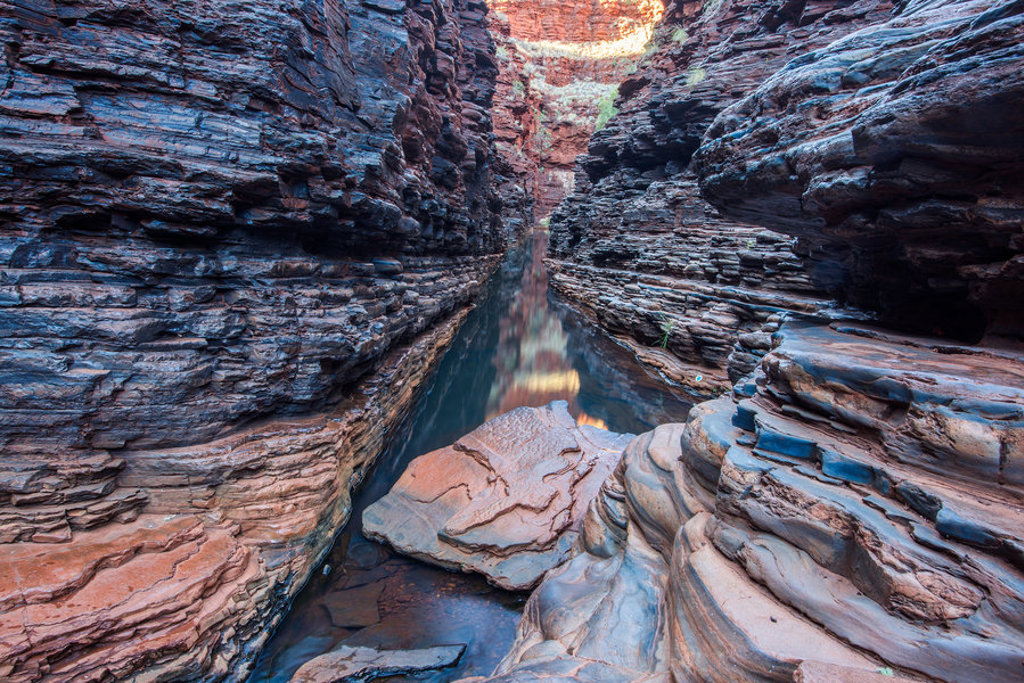 Smalle kloof met rotswanden en waterpoel in Karijini National Park, West-Australië.