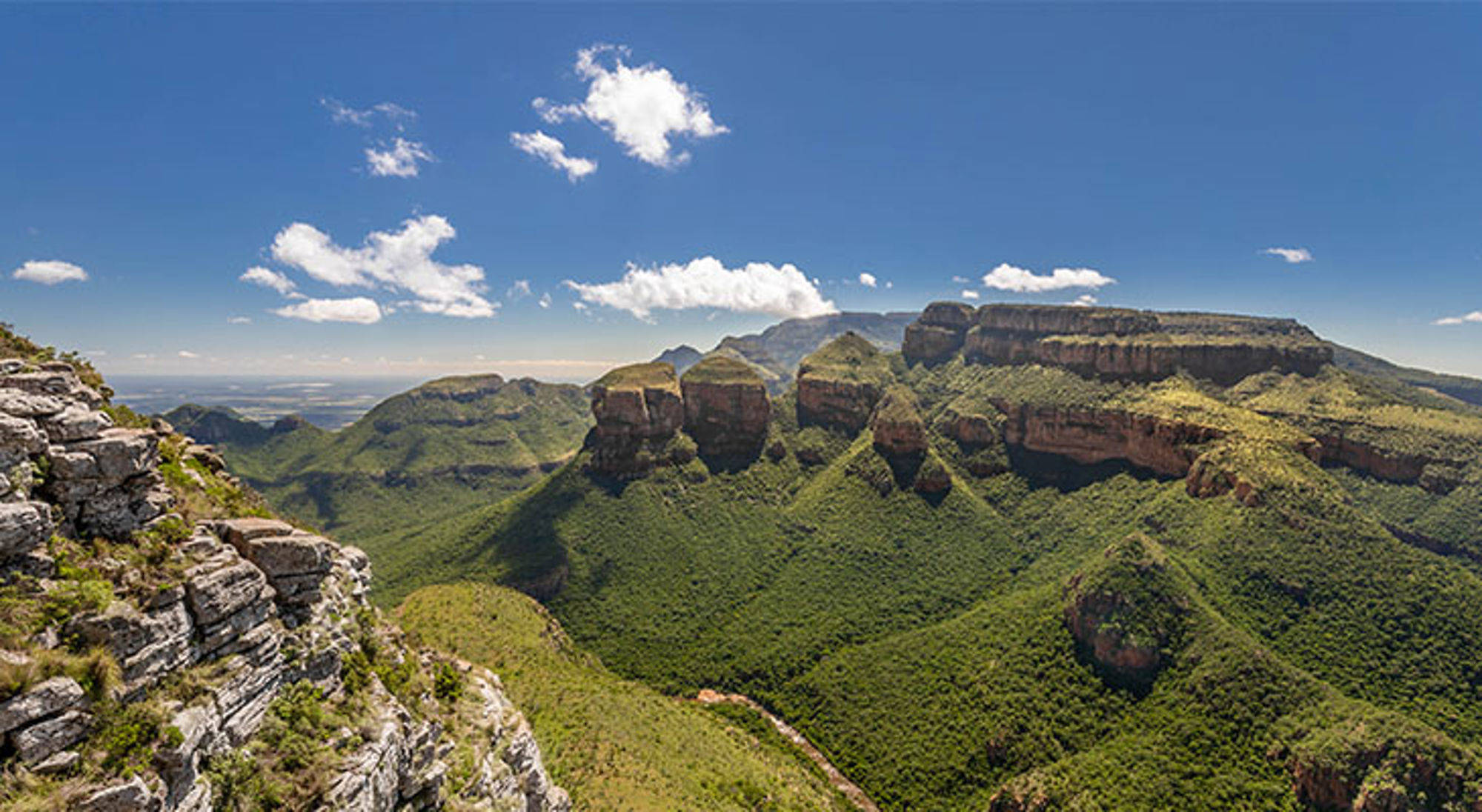 Uitzicht bij Gods Window Uitzicht op de Three Rondavels en Blyde River Canyon in Zuid-Afrika, met groene bergen en rotsformaties onder blauwe lucht.