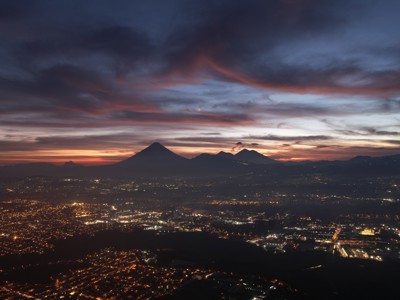 Zonsondergang boven Guatemala-Stad met silhouetten van vulkanen en fonkelende stadslichten.