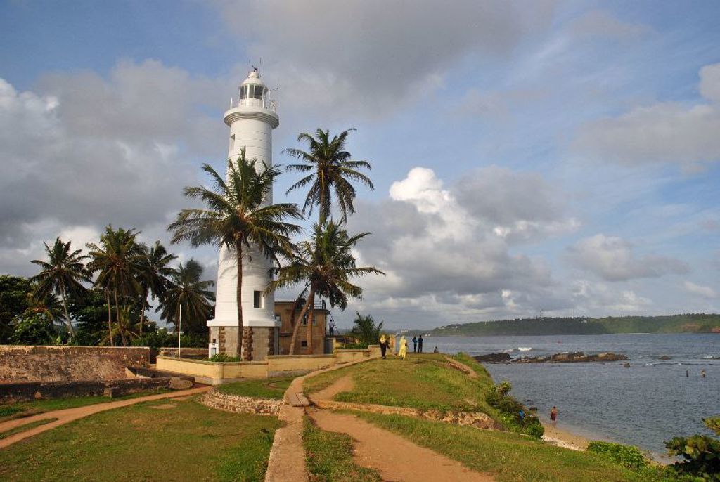 Witte vuurtoren bij Galle Fort aan de kust van Sri Lanka, omringd door palmbomen.